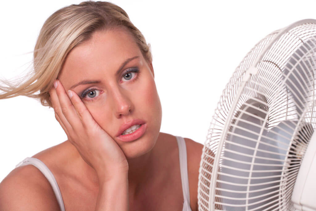 A young woman sits in front of a fan to cool off in a heatwave.